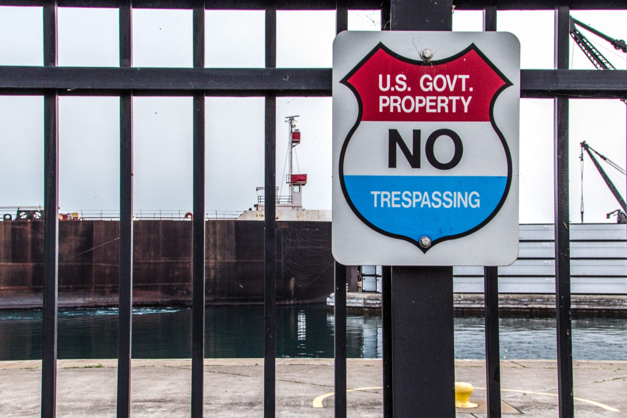 exterior photo of an electronic heavy-duty gate with a U.S. government no trespassing sign on it in front of ships